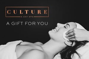 Smiling woman receives a relaxing spa treatment. Her face is being gently massaged at the temple while she lays on her back in a towel.